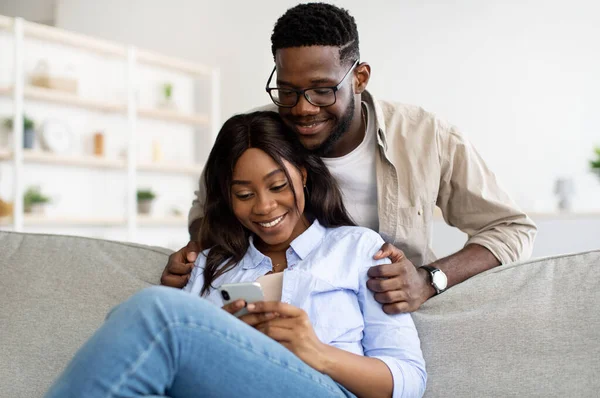 Африканська американська пара сидить на дивані, користуючись мобільним телефоном. — стокове фото