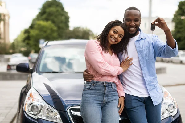 Feliz pareja negra apoyada en coche nuevo mostrando las llaves automáticas —  Fotos de Stock