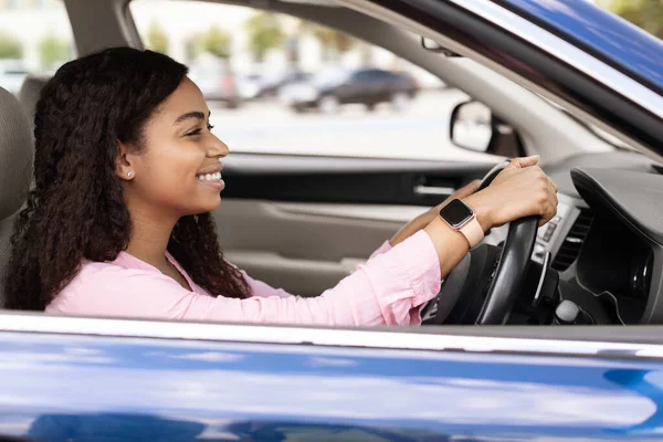 Smiling black female driving new car in city