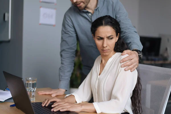Assédio no local de trabalho. Chefe masculino tocando sua jovem assistente feminina enquanto ela está trabalhando no laptop no escritório, espaço de cópia — Fotografia de Stock