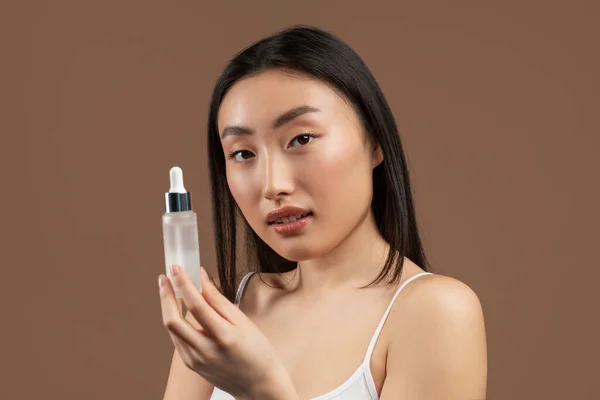 Hermosa mujer asiática joven sosteniendo botella con producto de belleza, utilizando suero antienvejecimiento en la rutina de belleza diaria — Foto de Stock