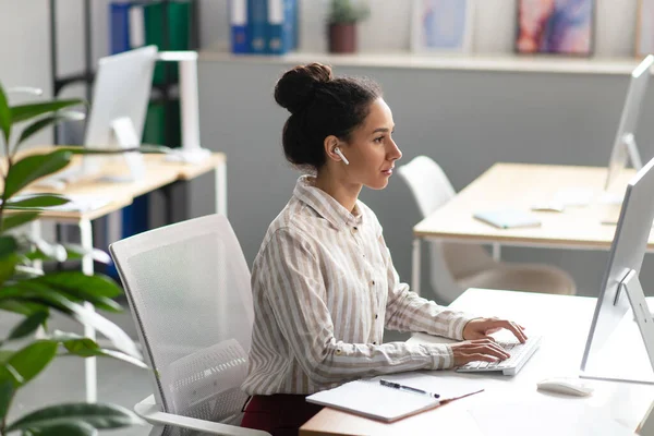 Trabajadora de oficina confiada que trabaja en la computadora moderna en la oficina, sentada en el lugar de trabajo, espacio libre — Foto de Stock