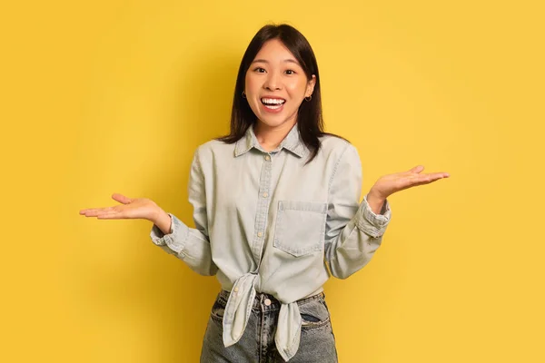 我不知道。困惑的年轻亚洲女人耸了耸肩，在黄色摄影棚的背景下对着相机微笑 — 图库照片