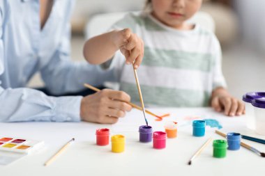 Çocuklar için sanat gelişimi. Anaokulunda öğretmeniyle resim yapan, renkli resimlerle resim çizen tanınmamış bir çocuk.