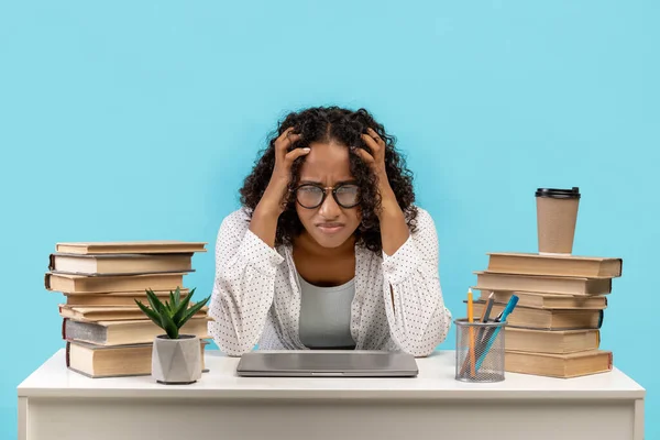 Infelice esausta studentessa nera seduta alla scrivania con libri e laptop, afferrando la testa, stanca di studiare — Foto Stock