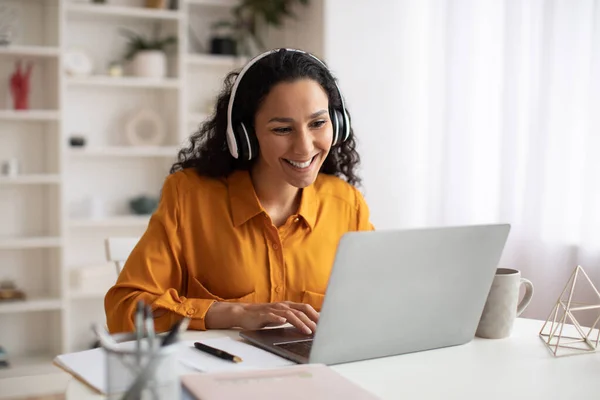 Glückliche brünette unternehmerin using laptop wearing headphones working at workplace — Stockfoto