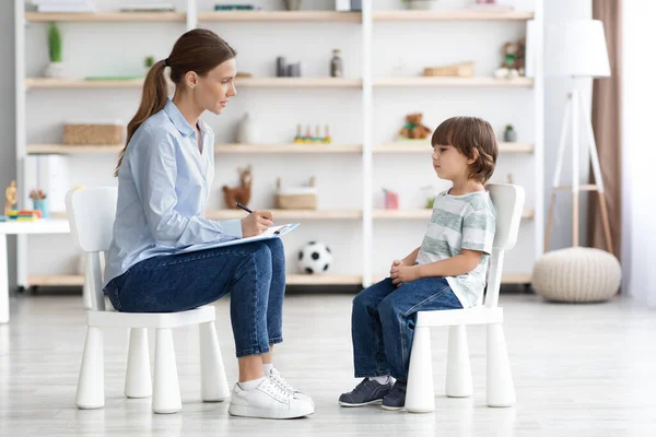 Психологічна консультація для дітей. Вид збоку знімок професійної жінки психотерапевт сидить проти маленького хлопчика — стокове фото
