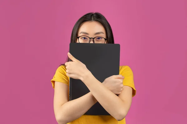 Asiática estudante em óculos escondidos atrás do laptop, estudando para exames universitários on-line, de pé sobre fundo violeta — Fotografia de Stock