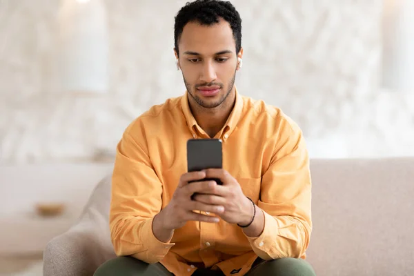 Hombre árabe joven usando teléfono celular usando auriculares —  Fotos de Stock
