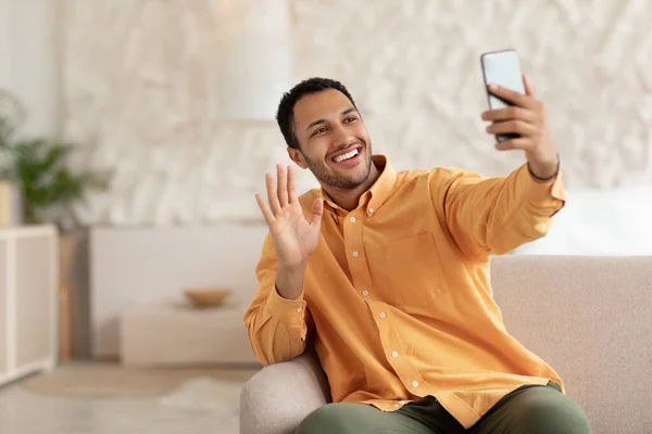 Smiling young man waving hand using mobile phone — ストック写真