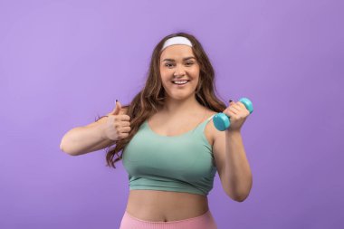 Bin yıllık Avrupalı ve spor giyim bölümünde beden ölçülerinde bir kadının dambıllarla egzersiz yapmasına ve baş parmağını kaldırmasına sevindim.