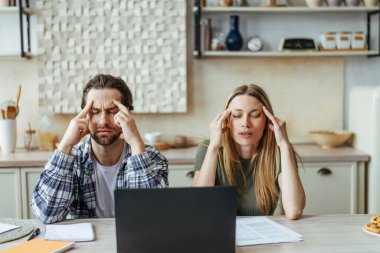 Mutsuz genç Avrupalı çift stresli, düşünceli ve baş ağrısı çekiyor, faturaları ödüyor ve dizüstü bilgisayarla vergi ödüyor