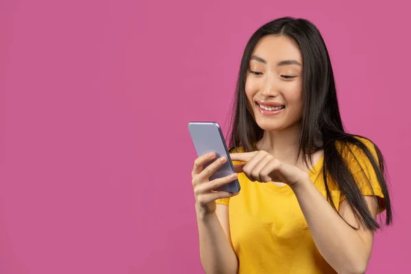 Vrolijke Aziatische dame met behulp van smartphone voor berichten met vrienden, sms 'en op mobiele telefoon, violette achtergrond, vrije ruimte — Stockfoto