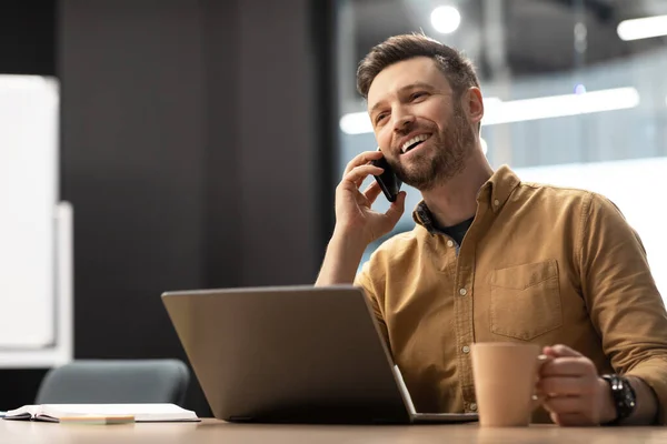 Business Guy Talking On Phone Using Laptop Sitting At Workplace