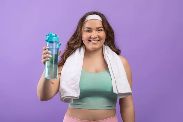 Gelukkig jong europees plus size vrouw in sportkleding met handdoek tonen fles water — Stockfoto