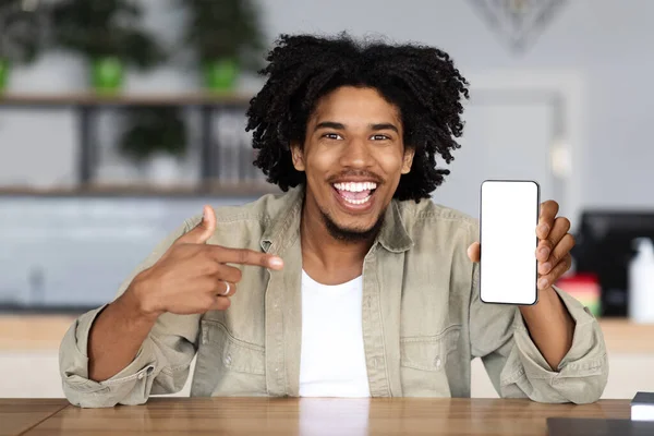 Feliz millennial africano americano rizado hombre apuntando con el dedo al teléfono inteligente con pantalla en blanco —  Fotos de Stock