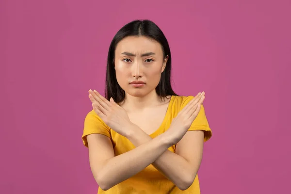 Portrait of serious asian lady showing stop gesture with crossed hands, posing over violet studio background — 스톡 사진