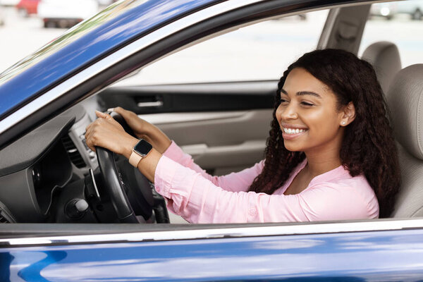 Smiling black lady driving new car in city