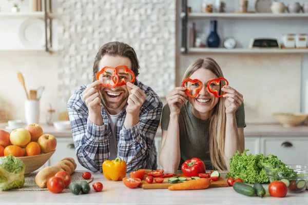 Jsem rád, že vtipný mladý evropský pár vaří u stolu s organickou zeleninou, bavte se a dát kousky pepře na oči — Stock fotografie