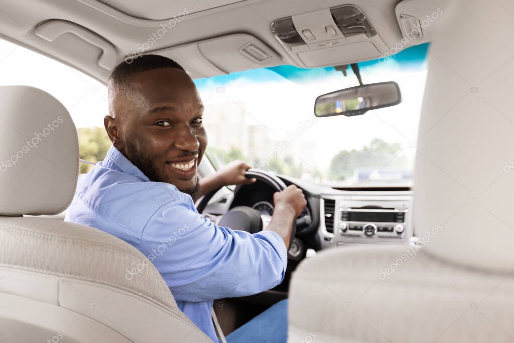 Smiling black man driving new car in city turning back