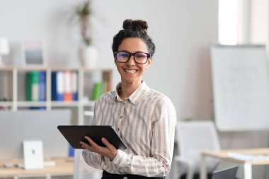 Dijital tablet tutan mutlu girişimci genç kadın, modern teknolojileri iş dünyasında ve ofis içinde kullanıyor.