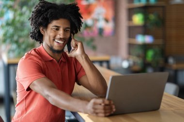 İyi ki Afro-Amerikan kıvırcık erkeği telefonla arıyor. Kafenin içindeki masada dizüstü bilgisayara bakıyor.