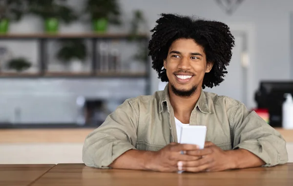 Happy young handsome african american curly male blogger student typing on phone at table — 스톡 사진