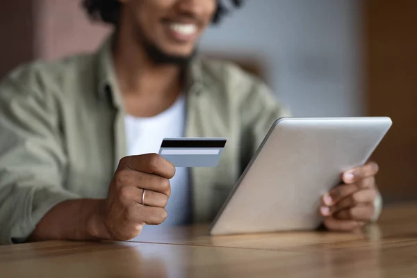 Vágott boldog millenniumi afro-amerikai srác táblagép ül az asztalnál, és tartsa a hitelkártya fizetni — Stock Fotó