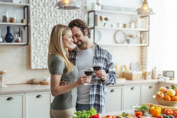 Kirli sakallı gülümseyen Avrupalı genç bir adam ve kadeh tokuşturan bir kadın, mutfakta hassas anın tadını çıkar. — Stok fotoğraf