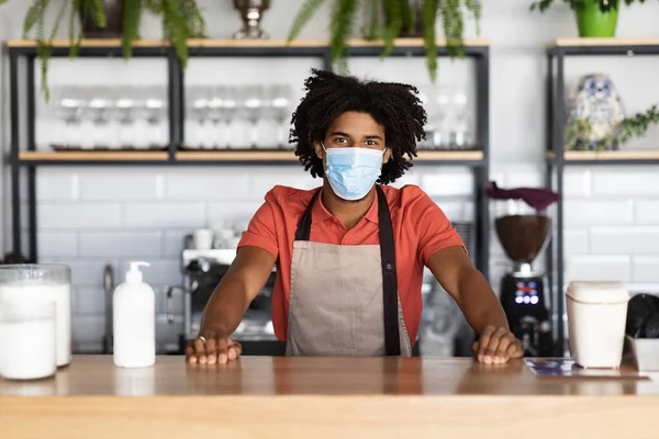 Glücklich selbstbewusster junger afrikanisch-amerikanischer Lockenkopf Kellner in Schutzmaske, Schürzenstand an der Theke im Café — Stockfoto