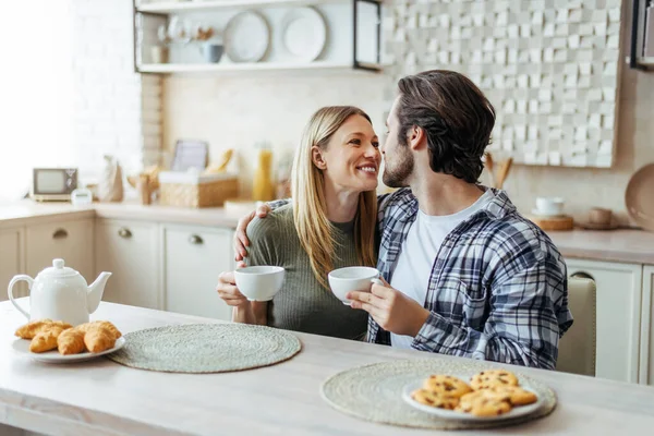 Boldog fiatal kaukázusi pár egymásra néznek, teát isznak, hétvégén a modern konyhában töltik a szabadidejüket. — Stock Fotó
