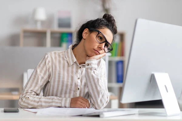 Porträt einer gelangweilten Geschäftsfrau, die am Schreibtisch sitzt, den Kopf in die Hand lehnt und auf den Computermonitor blickt — Stockfoto