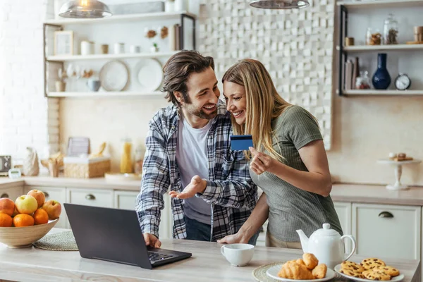 Kirli sakallı ve evli genç Avrupalı koca internetten alışveriş yapıyor ve modern mutfakta kredi kartını gösteriyor. — Stok fotoğraf