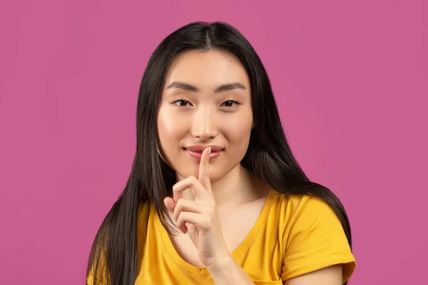 Geheimnisvolle asiatische Dame hält Finger in Lippennähe und schaut in die Kamera, hübsche Frau macht shh Geste — Stockfoto