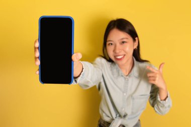 Pozitif Asyalı kadın akıllı telefon ile modelleme yapıyor, yeni uygulama ya da web sitesi reklamları yapıyor, ürünü tanıtıyor