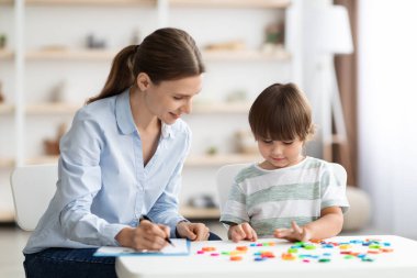 Profesyonel öğretmenle okumak için sevimli küçük çocuk, pozitif kadın öğretmen çocuğa yardım ediyor ve notlar alıyor.