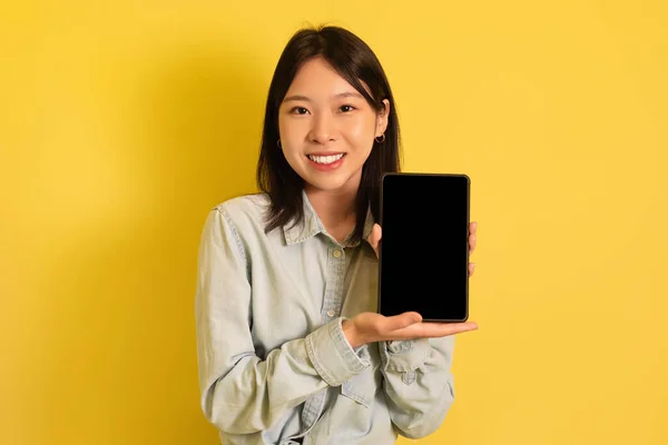 Millennial Asian Lady präsentiert Attrappe für Werbung auf Tablet-Bildschirm über gelbem Studiohintergrund — Stockfoto