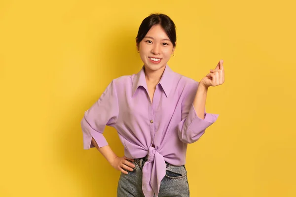 Feliz jovem ásia senhora segurando invisível objeto na mão no amarelo estúdio fundo, mockup — Fotografia de Stock