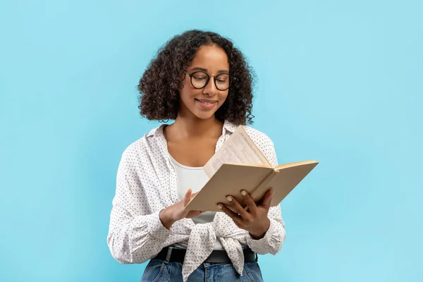 Szczęśliwy czarny uczennica czytanie podręcznika, co domowe zadanie, nauka do egzaminu na tle niebieskiego studia — Zdjęcie stockowe