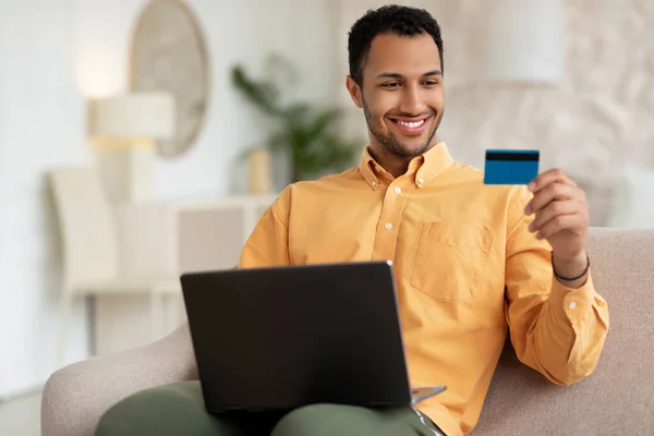 Hombre sonriente usando PC y tarjeta de crédito en casa — Foto de Stock