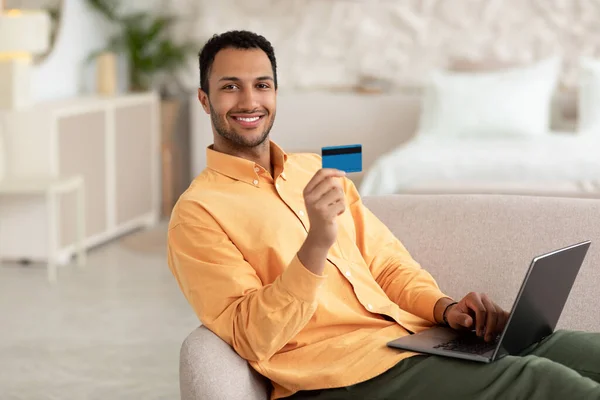 Hombre alegre usando PC y tarjeta de crédito en casa —  Fotos de Stock