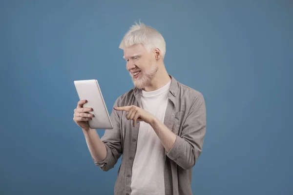 Gündelik kıyafet giyen, dijital tablet kullanan, çalışan veya internetten okuyan, e-posta gönderen, mavi arkaplan kullanan pozitif albino adam — Stok fotoğraf