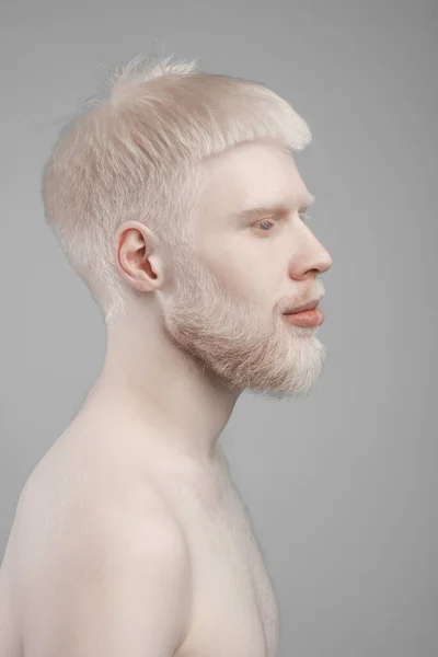 Profil-Porträt eines jungen bärtigen Albino-Mannes mit nackten Schultern, der vor grauem Studiohintergrund posiert — Stockfoto