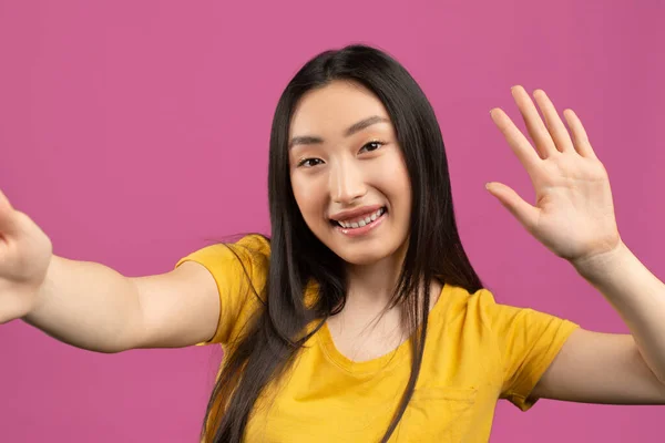 Jó napot! Boldog koreai hölgy csinál szelfi és integető kéz a kamera, gesztikuláló hi miközben fénykép át lila háttér — Stock Fotó