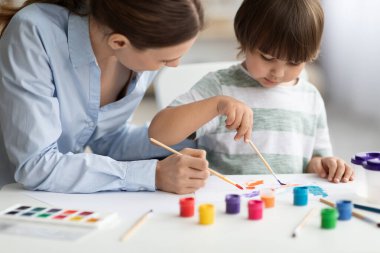 Anaokulu öğrencileri için sanat dersleri. Ders sırasında küçük çocuğun resim yapmasına yardım eden profesyonel kadın öğretmen.