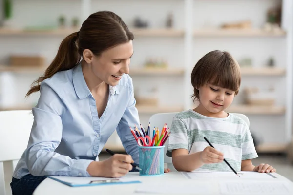 Konstutveckling. Talangfull liten pojke rita bild med färgglada pennor, omtänksam kvinna psykolog titta på barn — Stockfoto