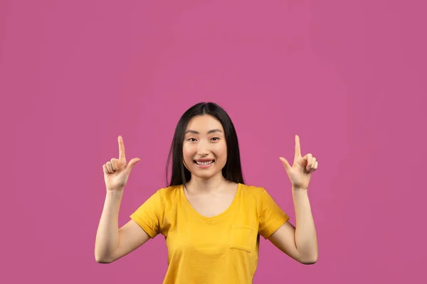 Alegre mujer asiática señalando hacia arriba con ambas manos y sonriendo a la cámara, señora feliz mostrando espacio libre para la publicidad — Foto de Stock