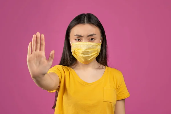 Stop de covid-19 pandemie. Jonge aziatische vrouw met medisch beschermend masker en uitgestrekte hand, violette achtergrond — Stockfoto