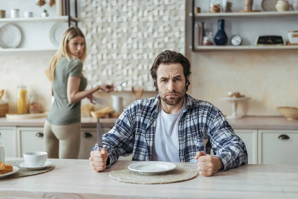 Kızgın aç, tatminsiz bin yıllık, sakallı beyaz bir adam. Kadınları görmezden geliyor ve mutfakta yemek bekliyor. — Stok fotoğraf