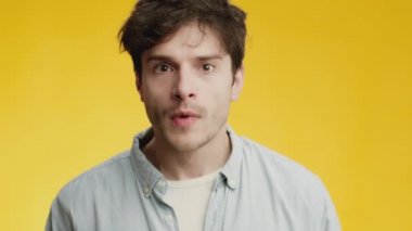 Genç adam kameraya dikkatlice bakıyor ve şok olmuş hissediyor, ağzı açık bir şekilde şaşkınlıkla yüzüne dokunuyor.